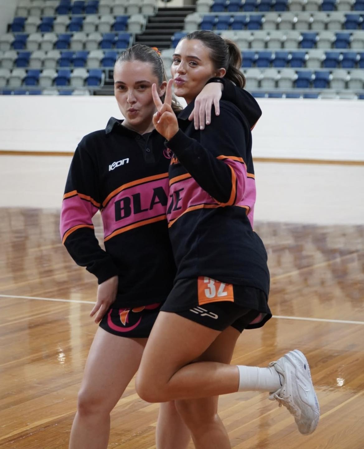 Two netball players wearing black, pink and orange ICON warm-up apparel